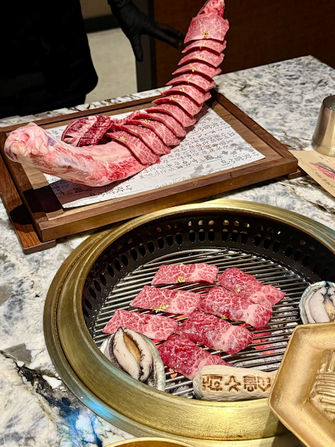 불판 위에서 노릇하게 익어가는 한우 갈비와 양념 갈비, 그리고 그 옆에 놓인 신선한 전복과 버섯