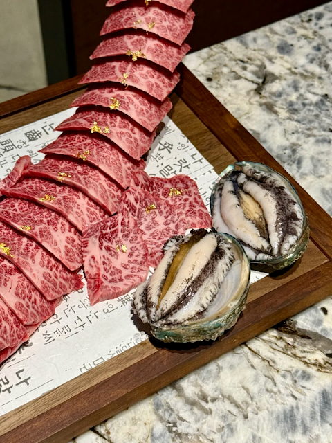 두툼하게 썰린 한우 갈비와 싱싱한 전복 두 마리가 고급스러운 접시에 담겨져 있는 모습
